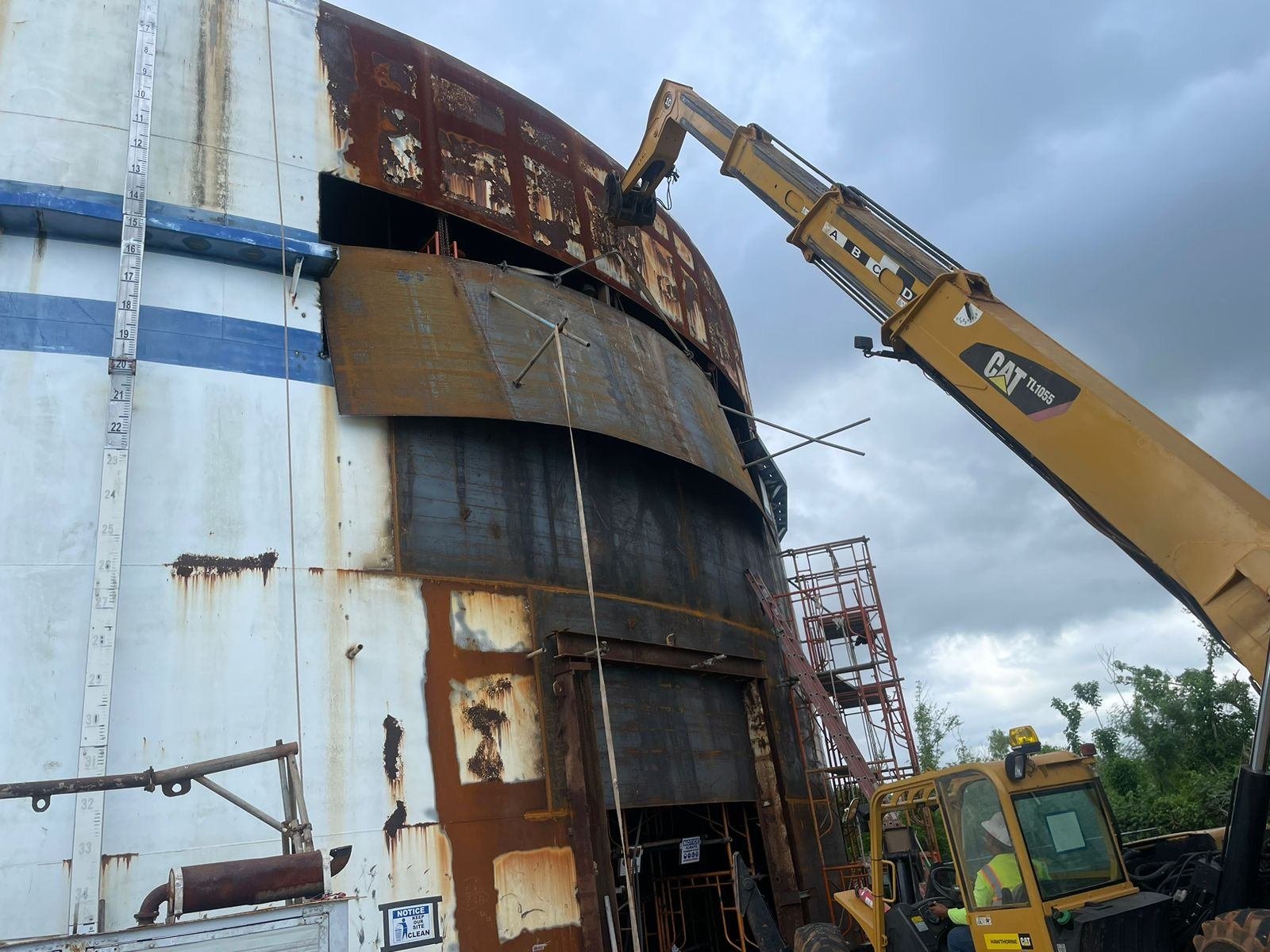 Excavator lifting a curved steel shell plate on the Astumbo tank