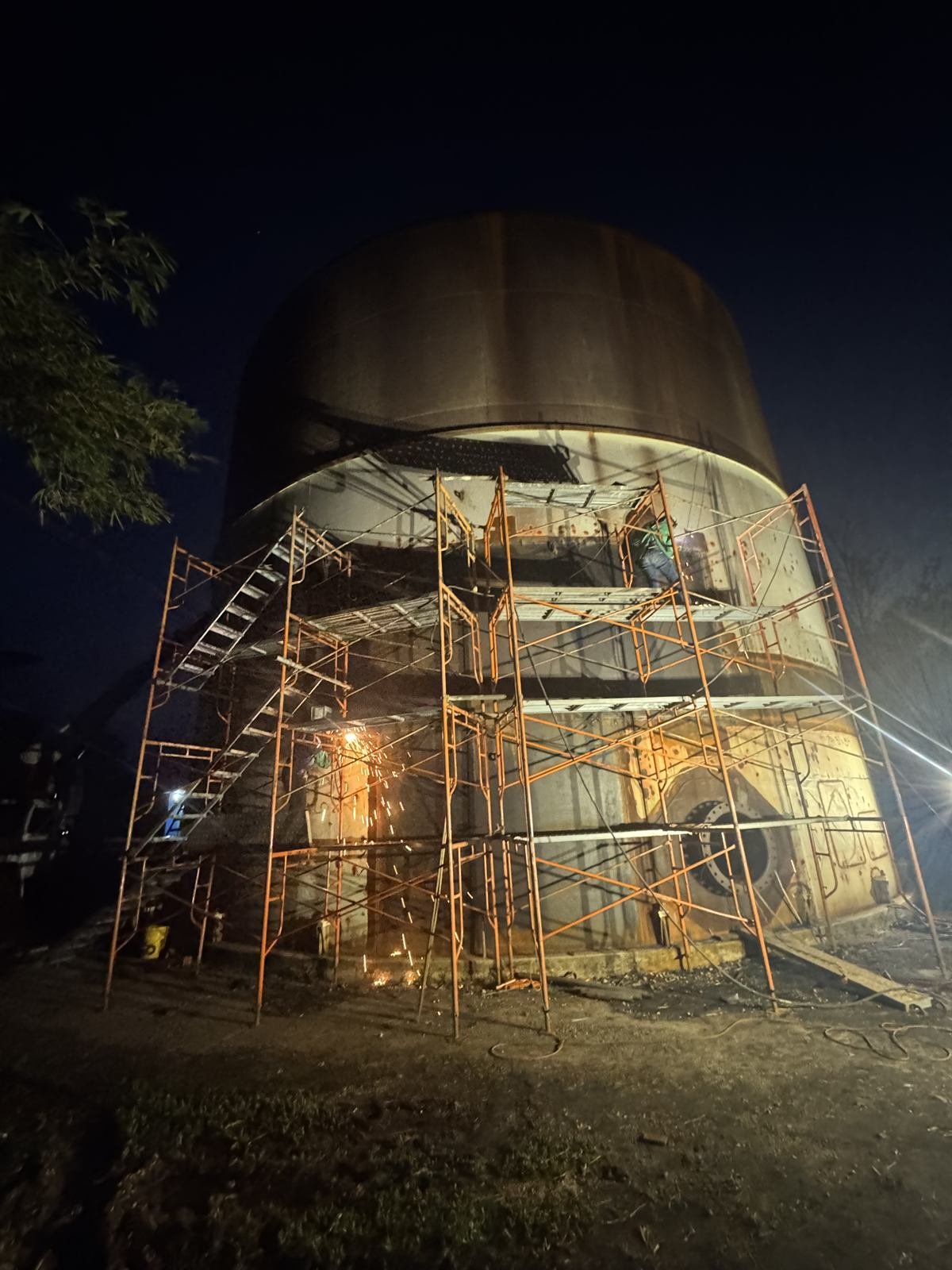 Welding crew working at night on scaffolding around a tank